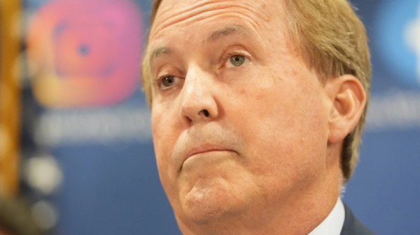 Close-up of a middle-aged man in a suit looking upward with a serious expression against a blue background.