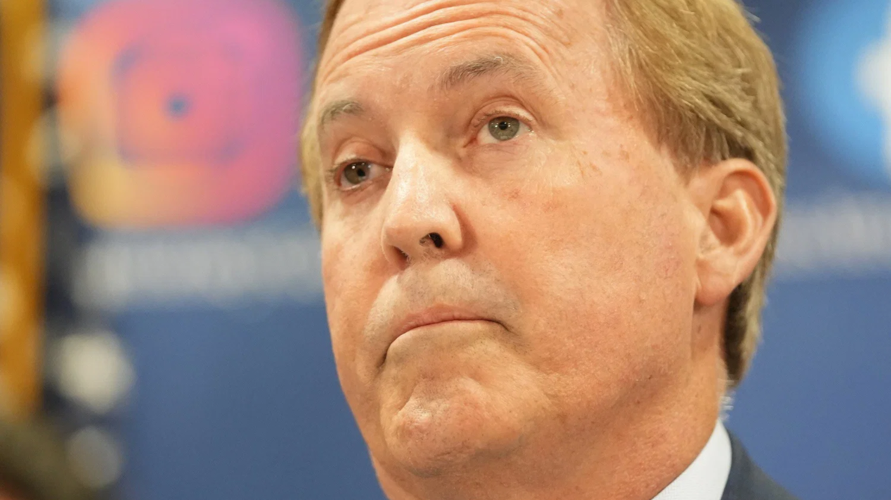 Close-up of a middle-aged man in a suit looking upward with a serious expression against a blue background.